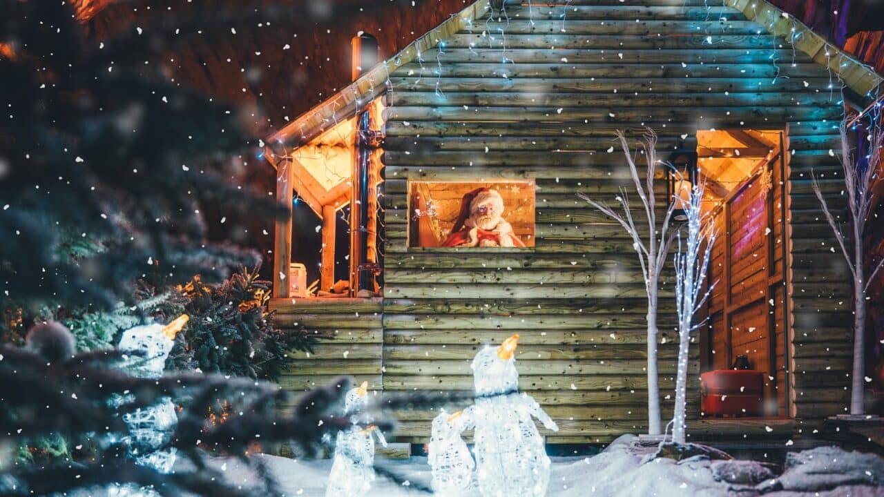 Santa sitting in a wooden hut with lit up penguins in front